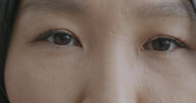 Close-up slow motion portrait of beautiful young Asian woman's eyes looking at camera with no emotion. Face expression and people concept.