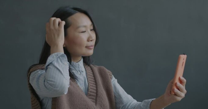 Slow motion portrait of beautiful Asian woman posing for smartphone camera taking selfie on black color background. People and photo concept.