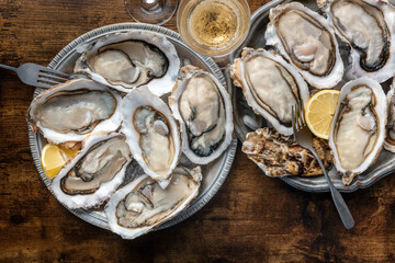 Fresh raw oysters on ice, two platters, shot from the top, with champagne and lemon slices, on a rustic wooden table