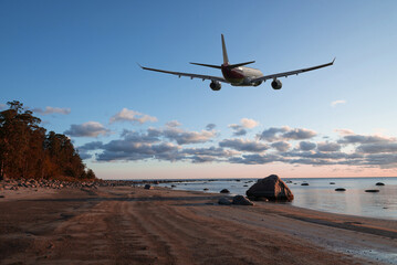 Airplane flying in sky with beautiful clouds over the coast at sunset time