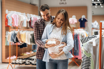 White cute little shoes. Pregnant woman with man are in the kid's clothing store