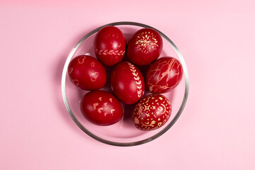 Red-painted Easter eggs on a glass plate on a pink background