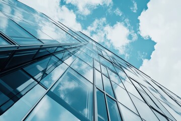 Modern glass skyscraper facade reflecting blue sky and clouds from low angle perspective in urban cityscape