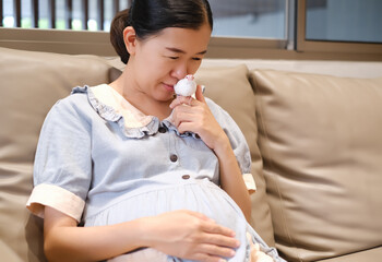 portrait asian young pregnant woman sit on the sofa bed with hand on belly and playing a white java sparrow small bird