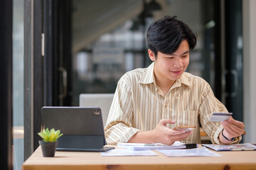 Fototapeta premium Businessman making an online purchase using smartphone and credit card at a modern office desk.