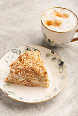 A slice of rich, layered dessert low calorie napoleon cake is presented on a floral plate alongside a cup of frothy coffee. 