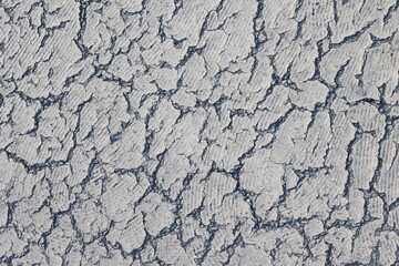 Texture of cracks and patterns of old white paint on bitumen on a  under bright daylight.