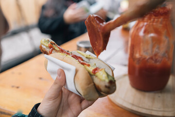 Bratwurst being topped with mustard and ketchup at a street food stall
