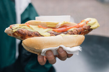 Hand holding a German sausage with mustard and ketchup