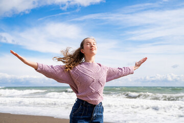 Young woman with open arms breathing fresh air on sand beach, practicing meditation in sunlight...