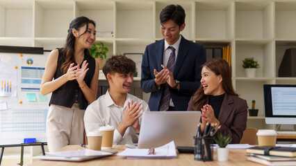 Group of happy business people clapping and smiling while looking at a laptop during a successful team meeting.