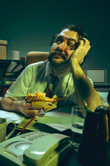 Daydreaming office worker holding sandwich, looks up with bored face at cluttered desk, showing...