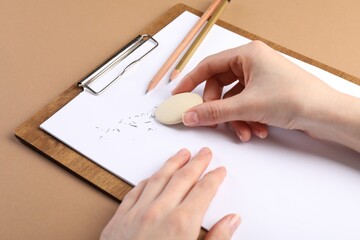 Woman rubbing eraser against paper at brown table, closeup