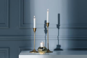 Stylish candlesticks with burning candles on white table near gray wall indoors