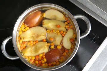 Making compot of apples and sea buckthorn berries. Simmering fruits in pot on stove, top view