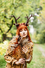 fairy woman with deer horns in autumn forest. Face painting. Beautiful mystery woman. redhead girl with big eyes magical sight
