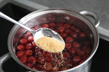 Adding sugar into tasty cherry compot in pot on stove, closeup