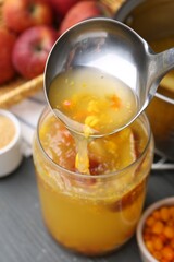 Pouring tasty compot into glass jar on grey wooden table, closeup