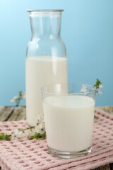 Fresh milk and blossoms on wooden table against light blue background, closeup