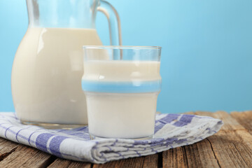 Fresh milk on wooden table against light blue background, closeup