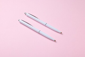 Ballpoint pens on pink background, above view