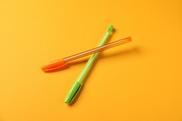 Stylish pens on orange background, above view
