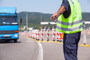 Highway traffic police officer wearing a reflective vest signals a blue truck to stop at a...