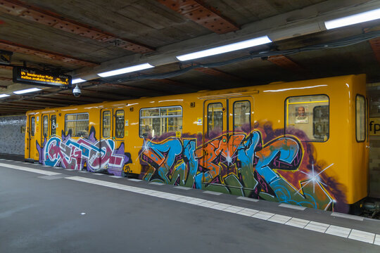 A yellow subway train car covered in vibrant graffiti art stands at a station platform with overhead lighting. Berlin, Germany. 28 March 2025.