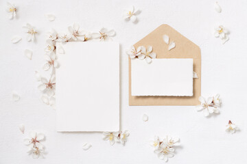 Blank cards and envelope near white cherry flowers top view, spring wedding mockup