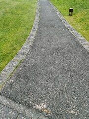 Obraz premium A winding concrete pathway cuts through green lawn in the park , bordered by trees and shrub . outdoor spaces for walk.laying of sidewalks with new asphalt.