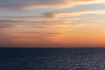 A serene sunset over the ocean with calm, dark waters below.