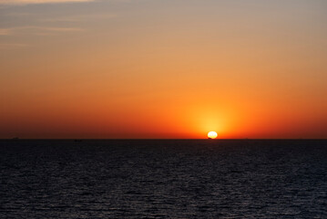 A serene sunset over the ocean with calm, dark waters below.