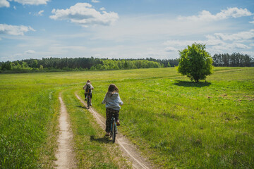 Mother and daughter, two cyclists ride through meadows, forest in Masuria. Spring, May, Poland.
