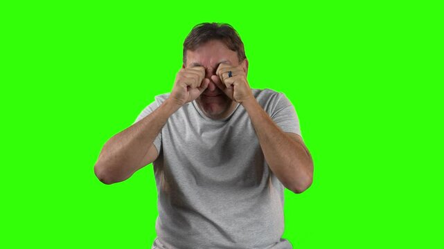 Man in gray t-shirt rubs his eyes as if crying or upset, expressing strong emotion or sadness. Captured on green screen, perfect for dramatic or humorous edits.  	
