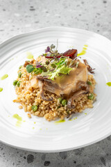 A gourmet dish with tender meat drizzled in rich gravy, served over rice mixed with peas and mushrooms, garnished with fresh greens and microgreens on a modern white plate.