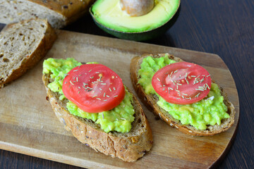 mashed Avocado with Tomato Slices on the slices of bread on cutting board