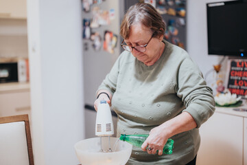 A senior woman mixes ingredients while cooking in a cozy kitchen environment. Performing delicate...
