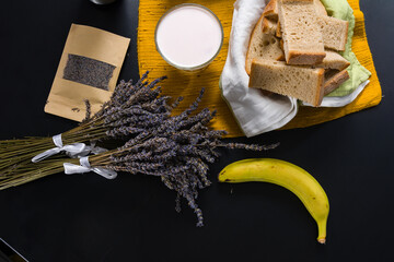 Flat lay of a simple breakfast setting featuring sliced bread, a banana, a glass of yogurt, dried...