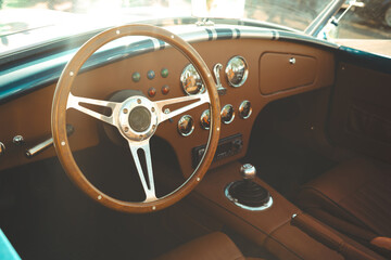 Vintage classic car interior featuring leather seats, chrome gauges, wooden steering wheel and polished dashboard