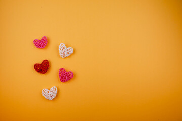 Five heart-shaped decorations in red, pink, and white are scattered on a vibrant orange background,...
