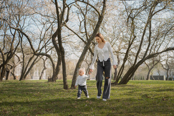 Fototapeta premium A happy family, a mother and child walking through the park holding hands in a city park on a sunny day. Parents, child, sun, nature