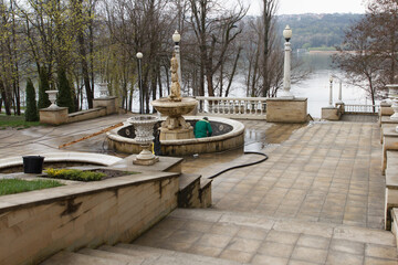 Worker cleaning an old stone fountain in a park during early spring day.
