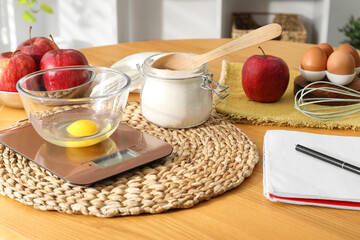 Electronic kitchen scale, products and stationery on wooden table indoors