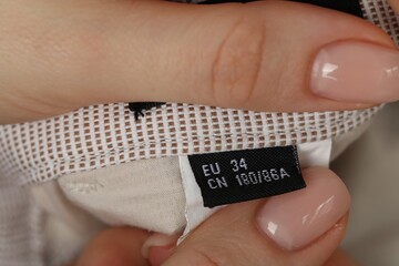Woman holding clothing label of light garment, closeup