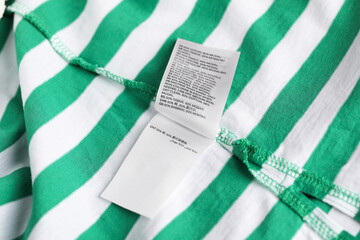 Clothing label on striped garment as background, closeup