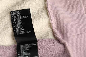 Clothing label with material content on color garment as background, above view