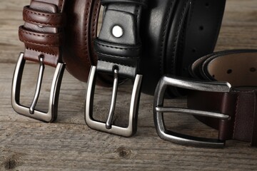 Three leather belts on wooden table, closeup