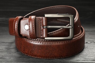 One brown leather belt on wooden table, closeup