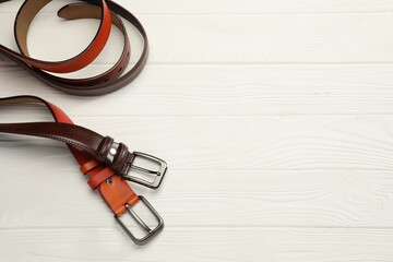 Two leather belts on white wooden table, above view. Space for text
