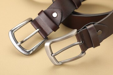 Two leather belts on beige background, closeup